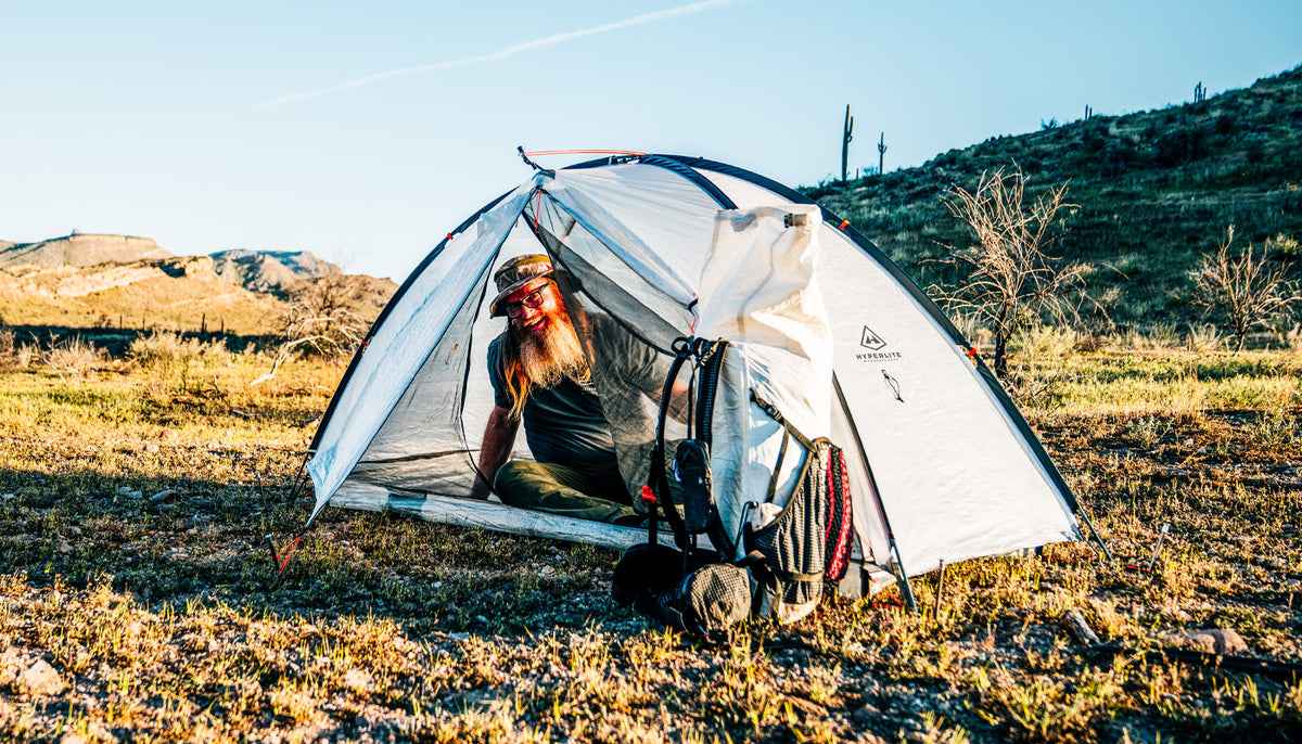 Person sitting inside a white camping tent in a desert landscape