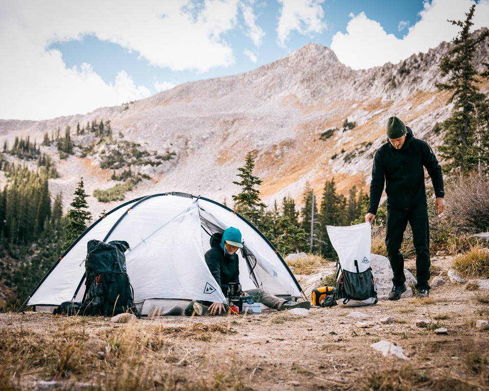 Two people setting up a tent in a mountainous outdoor setting.