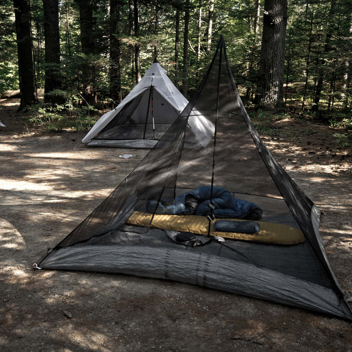 Exterior view of Hyperlite Mountain Gear Shelters UltaMid 2 Insert with DCF11 Floor without tent in a wooded setting. A white UltaMid 2 with insert sits in the background.