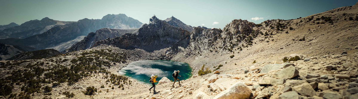 Two hikers near a mountain lake with a scenic mountain landscape.