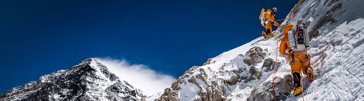 Two climbers on a snowy mountain peak with a clear blue sky.