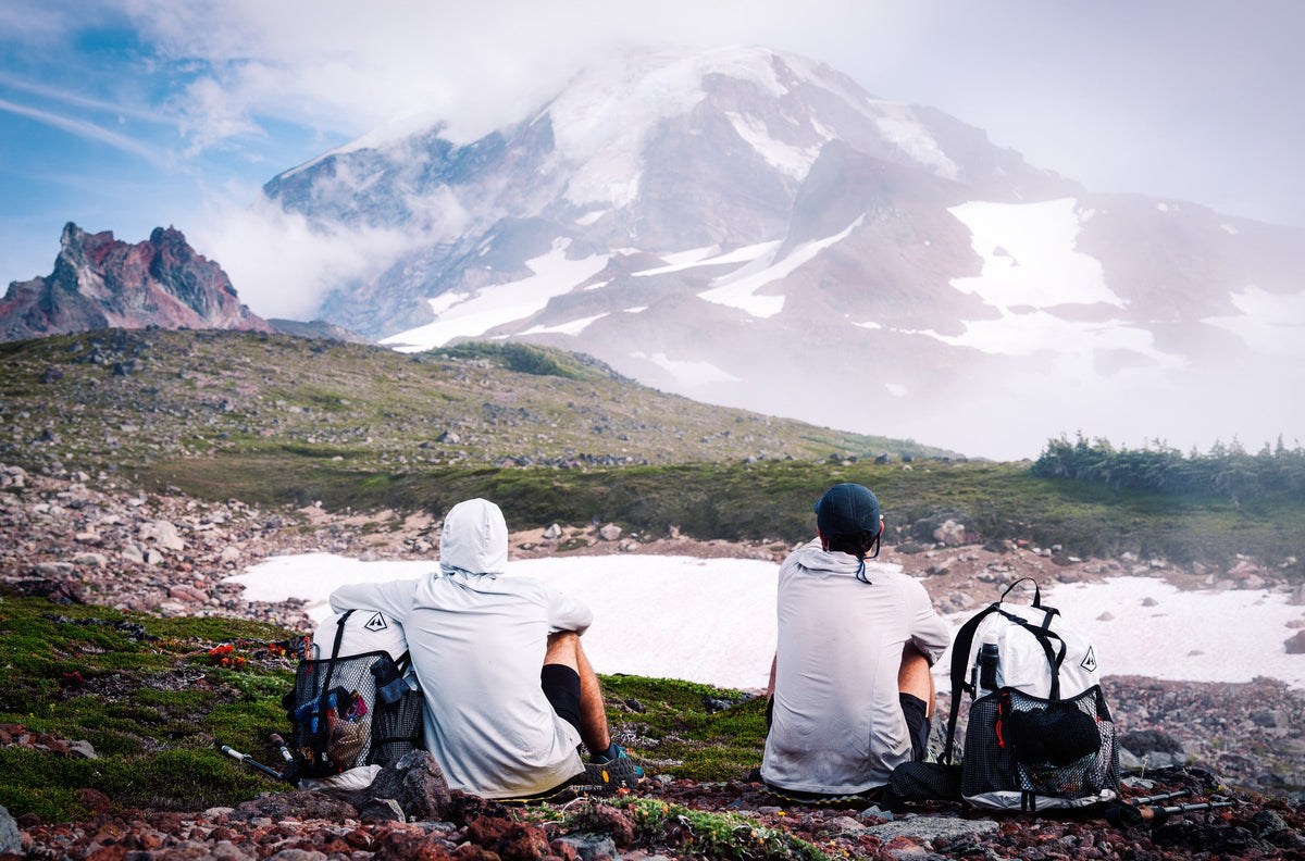Two people sitting on a rocky outcrop with a mountain in the background