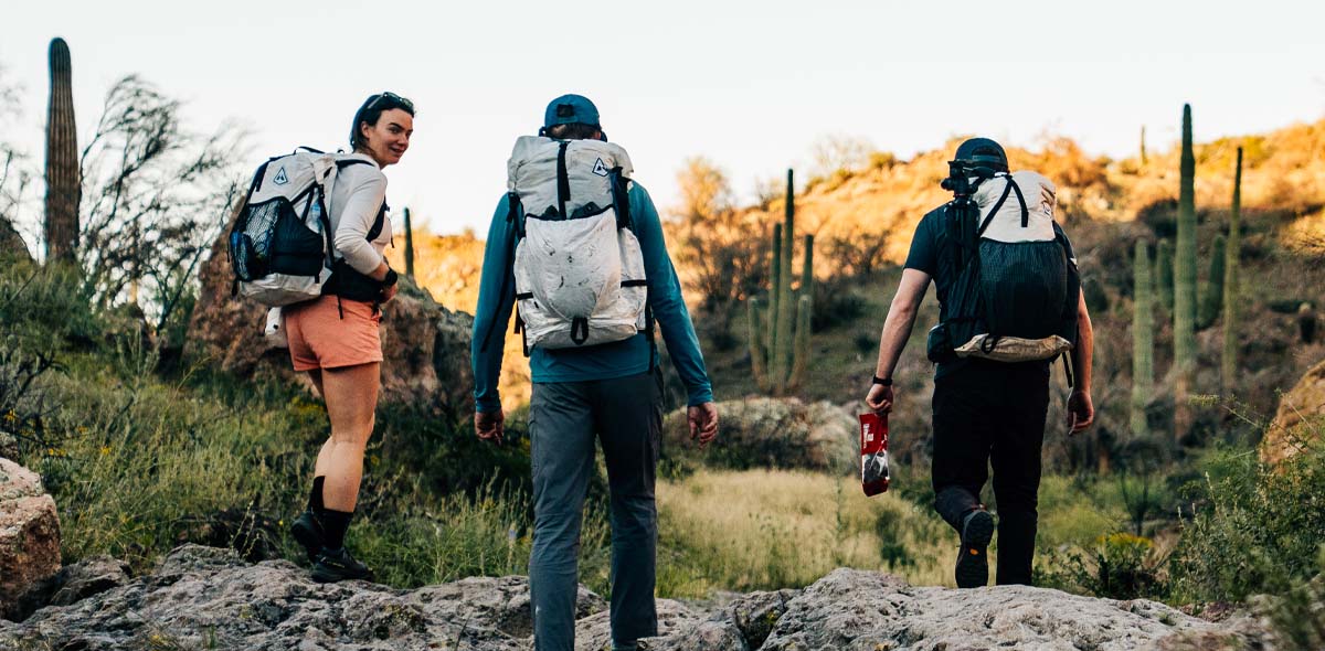 Three people hiking in a desert landscape with backpacks.