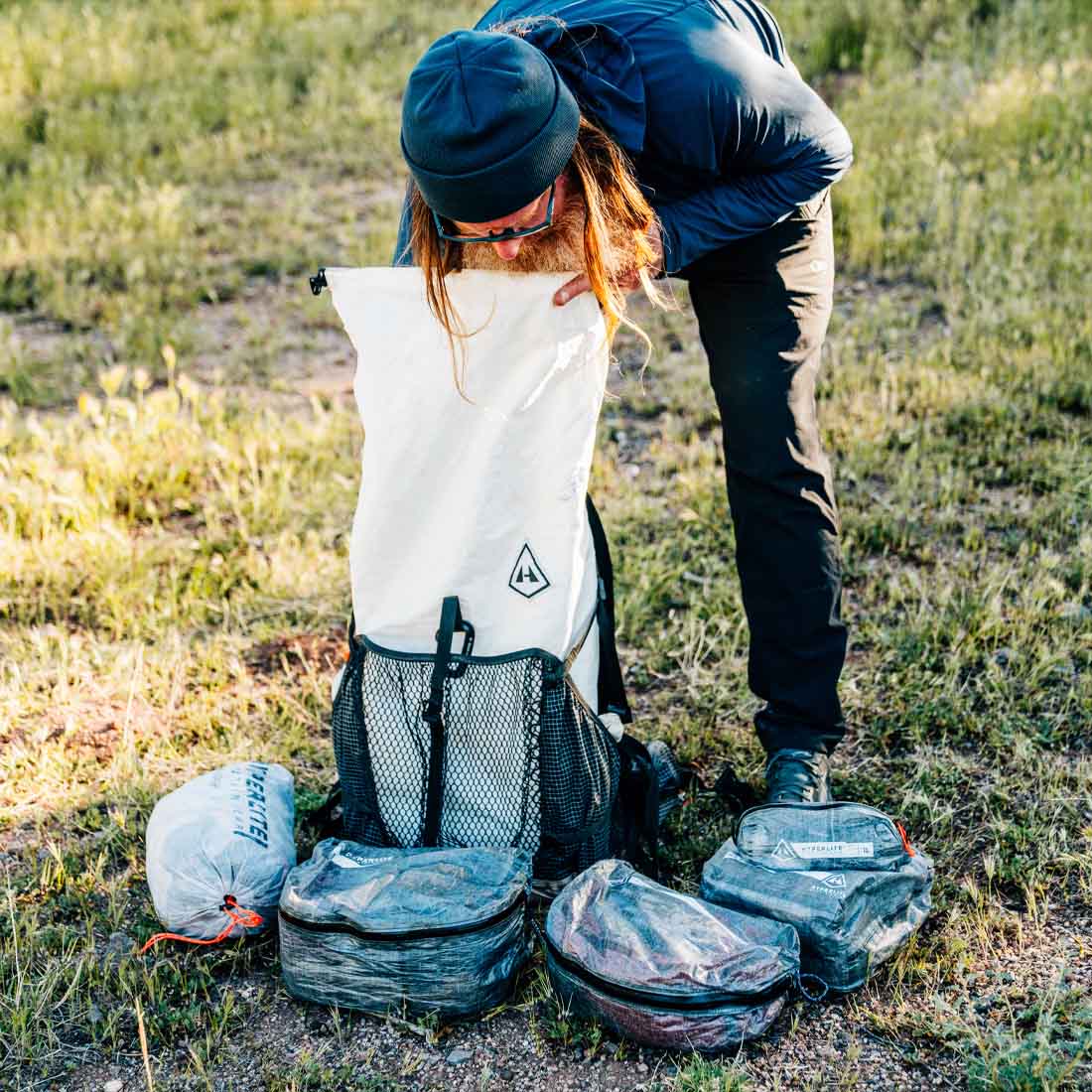 Person unpacking a large backpack in a grassy outdoor setting