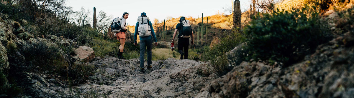 Three people hiking on a trail with backpacks in a natural setting