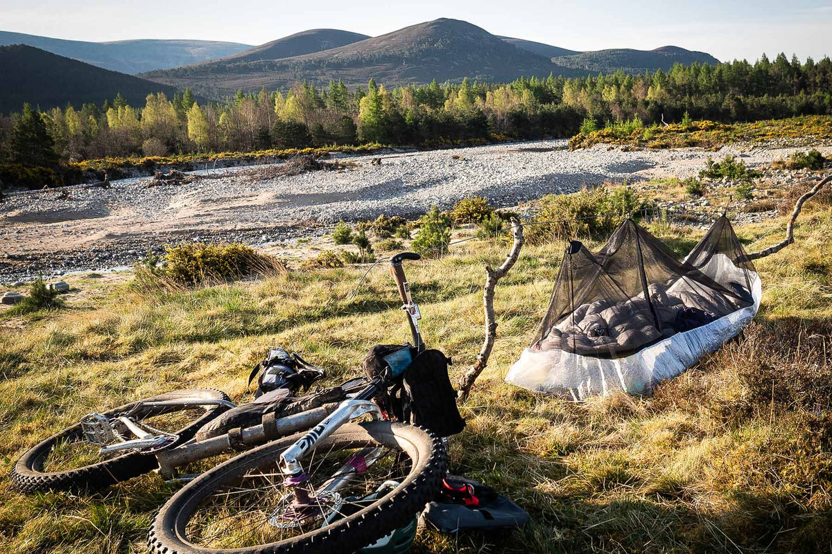 Bicycle and camping gear in a scenic outdoor setting with mountains and trees.