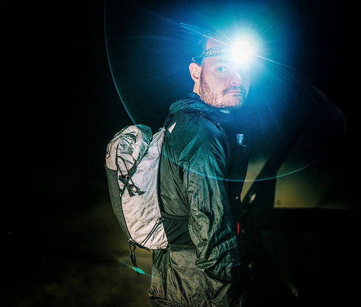 Person wearing a headlamp and backpack in a dark setting