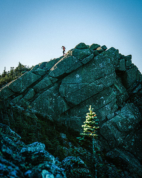 Person hiking down on a large rock formation with a clear blue sky