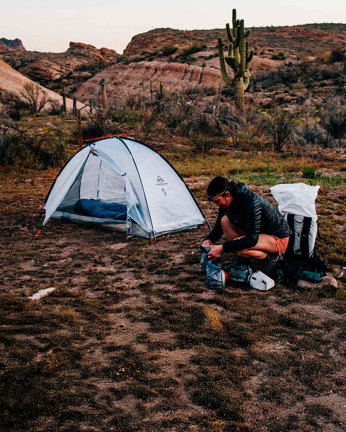 Person setting up camp near a tent in a desert landscape with cacti.