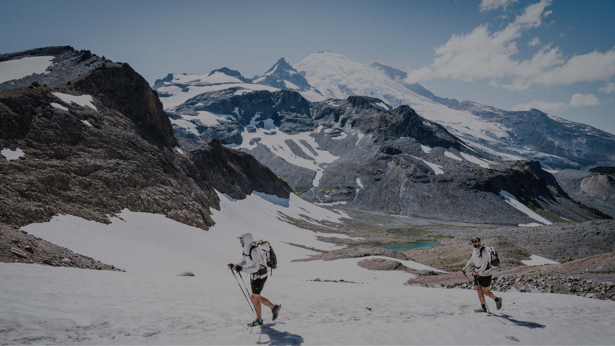 Two hikers on a snowy mountain with a large mountain range in the background