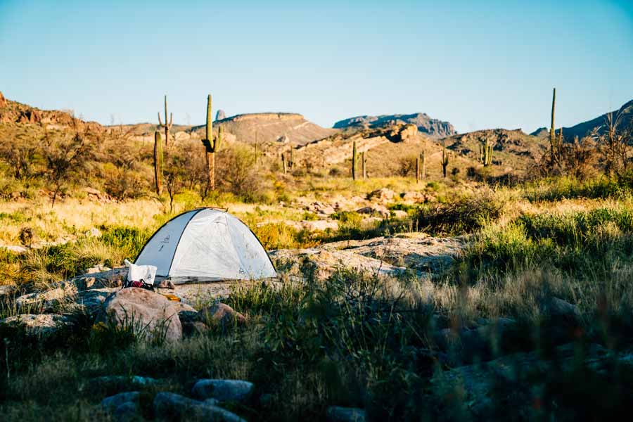 Camping tent in a desert landscape with mountains and cacti.
