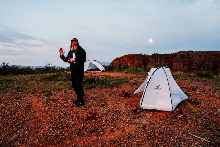 Person standing near two tents in a desert landscape with a moonlit sky.