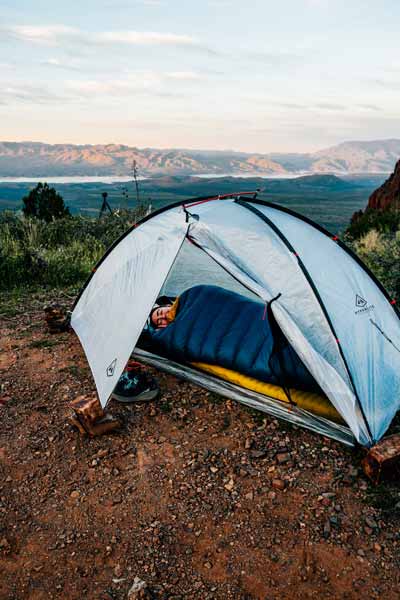 Person lying inside a camping tent with a scenic landscape in the background