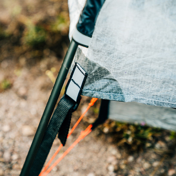 Close-up of a tent setup with a black pole and orange ropes on a natural background