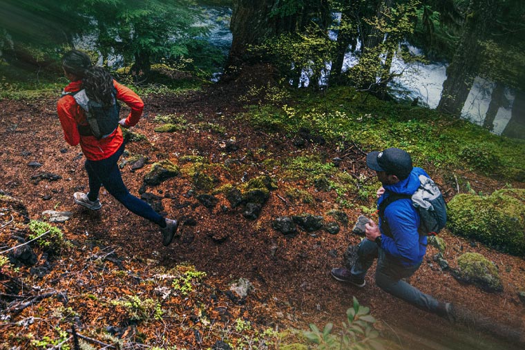 Two hikers on a trail in a forest with a lake in the background