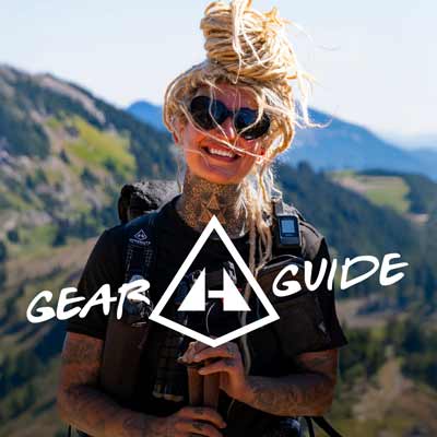Person with tattoos and sunglasses holding a phone, with 'Gear Guide' and Hyperlite Mountain Gear logo overlay, against a mountainous background.