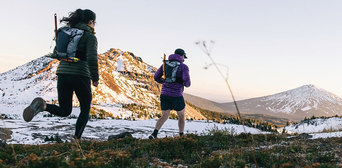 Two people hiking in a mountainous landscape with snow-capped peaks.