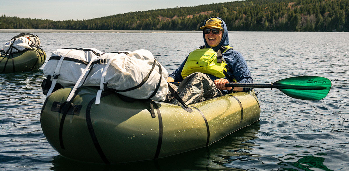Person paddling a kayak on a calm lake with trees in the background
