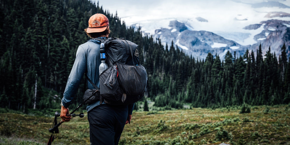 Hiker with a Southwest backpack and hat in a mountainous forest landscape.