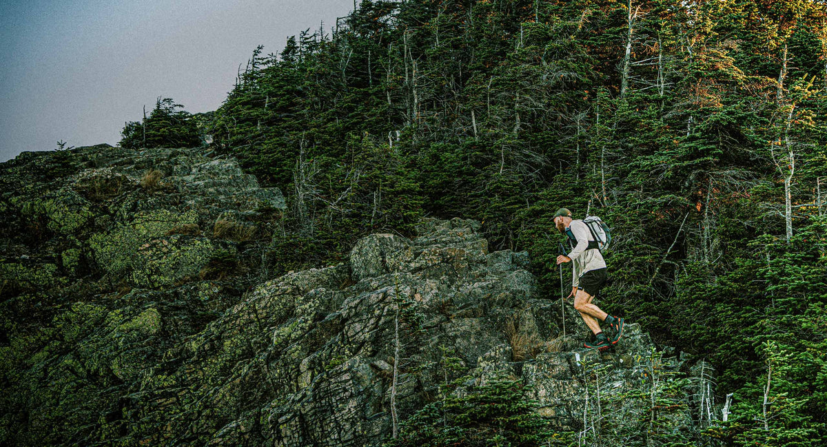 Person hiking on a rocky trail in a forested area with the Pemi 15 running vest