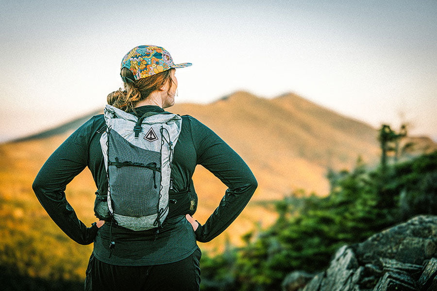 Person with a backpack and colorful cap standing in a mountainous landscape