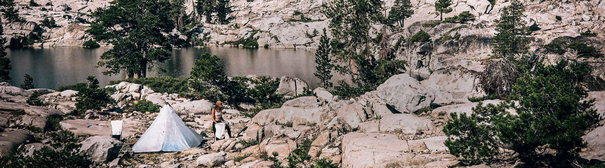 Camping scene with tents and a person in a rocky, mountainous area.
