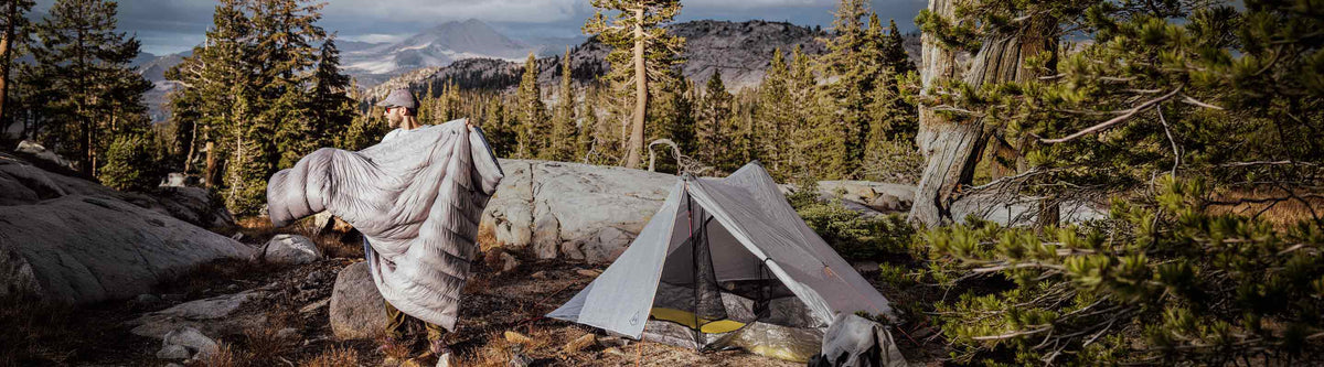 Tent set up in a forest with trees and mountains in the background