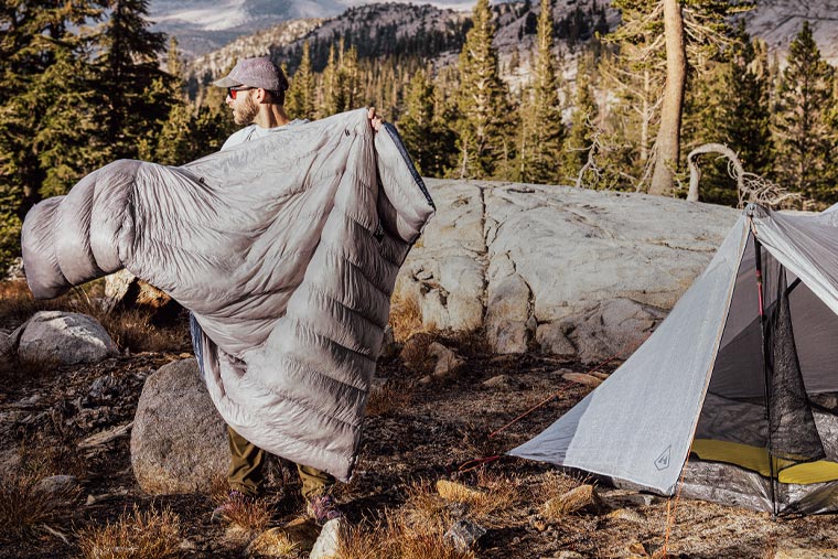 Person setting up a tent in a mountainous area with trees and rocks.