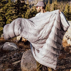 Person holding a large sleeping bag in a mountainous outdoor setting