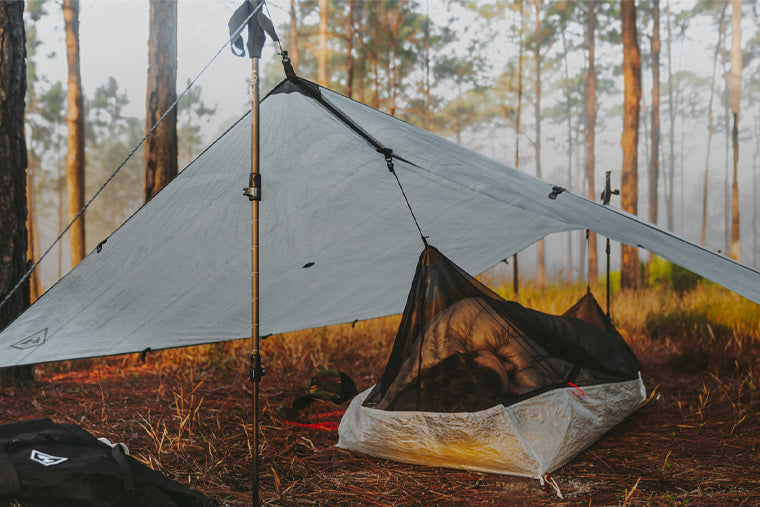 Camping tarp set up in a forest with a hammock