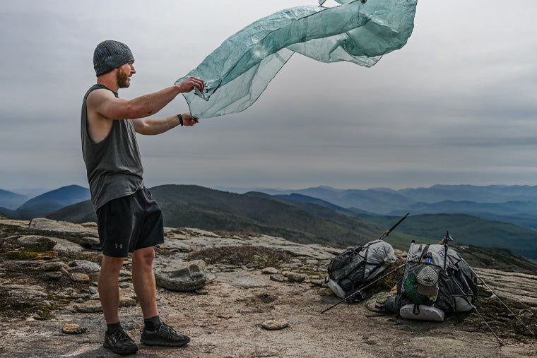 Man setting up a tent on a mountain top with backpacks nearby