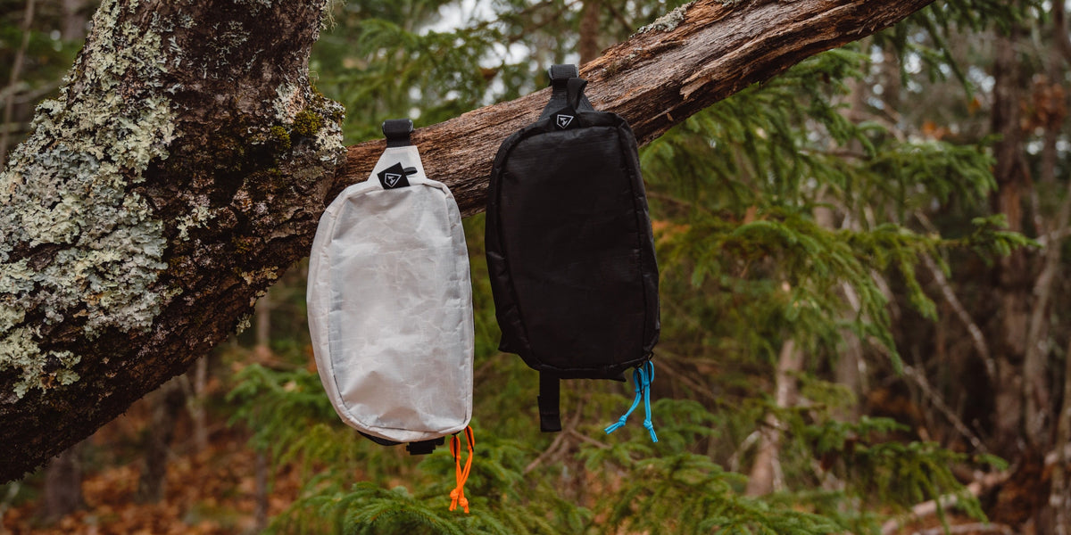 Two bags hanging from a tree in the woods.