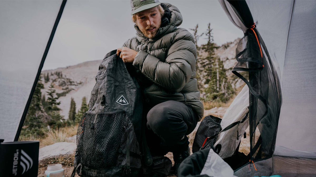 Man packing a backpack outdoors with mountains in the background