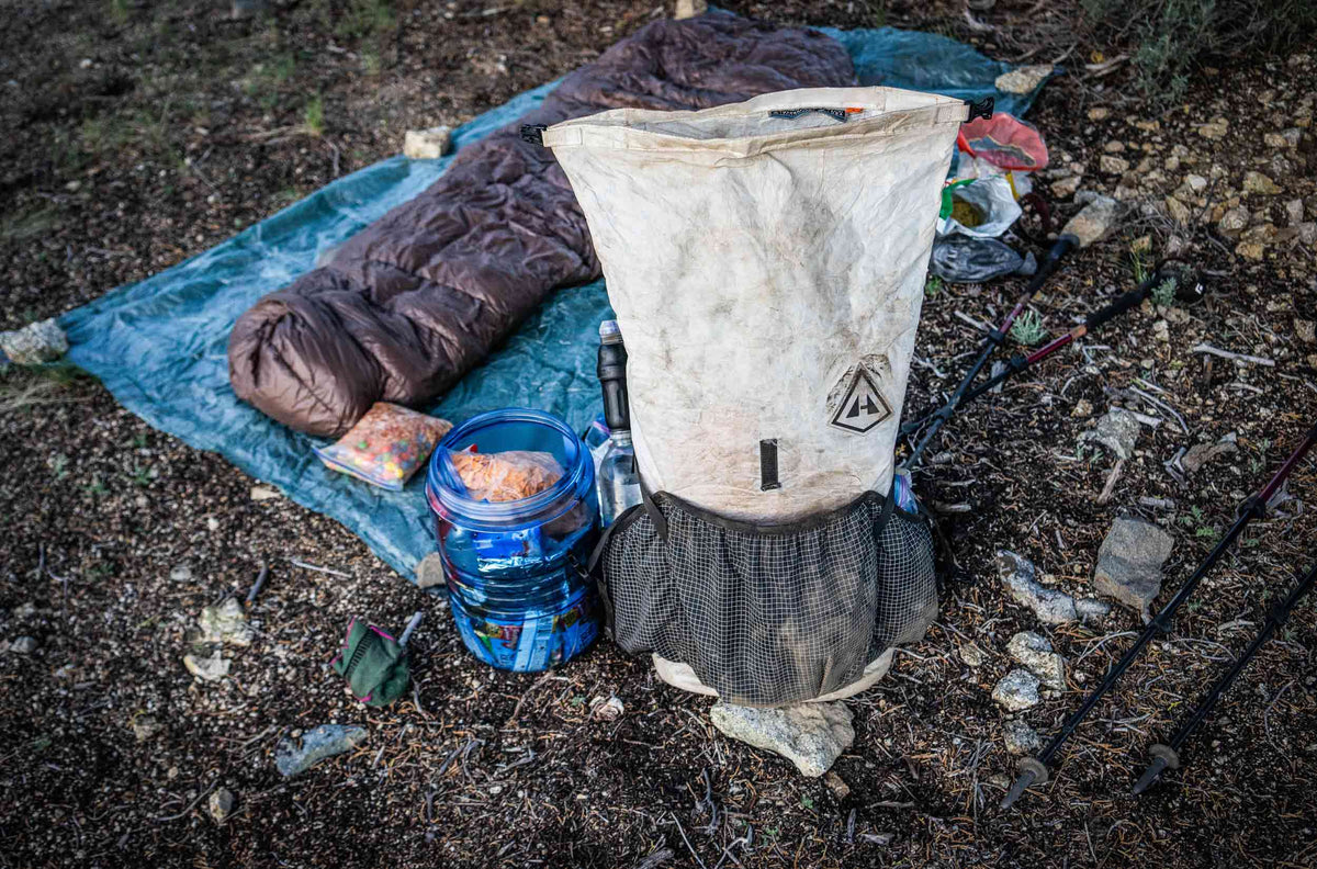 Hyperlite Mountain Gear camping gear including a sleeping quilt, floor mat, and food on a ground surface.